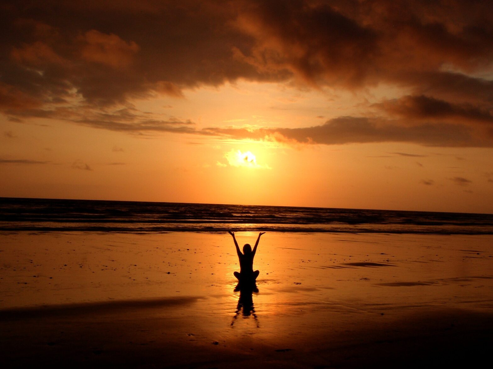 A silhouette of a person sitting on the sunset beach, attaining divine consciousness.